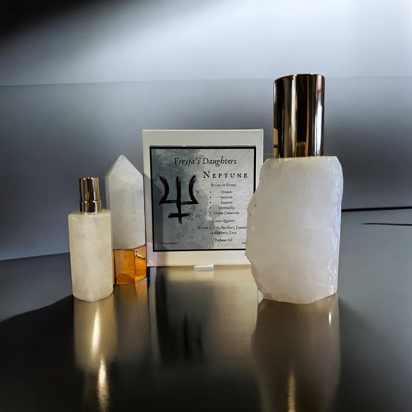 Collection of Freyja's Daughters Neptune perfume bottles, including a clear quartz roller ball, polished quartz spray bottle, and a large raw edge crystal bottle on a reflective surface.
