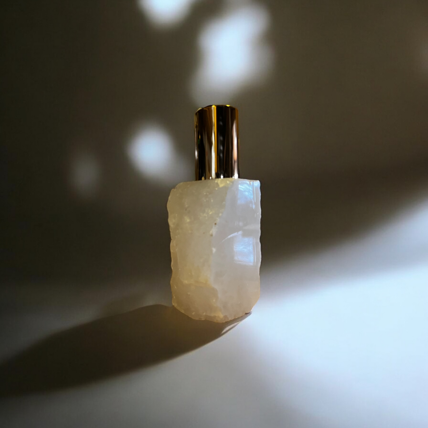 Close-up of a clear quartz bottle with a gold cap, casting a soft shadow against an illuminated background.
