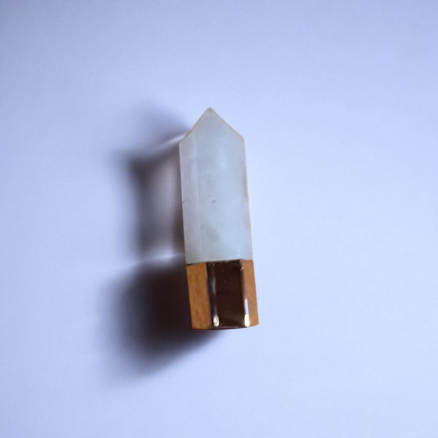 A polished quartz wand with a golden bottom, set against a plain white background, showcasing its elegant design.