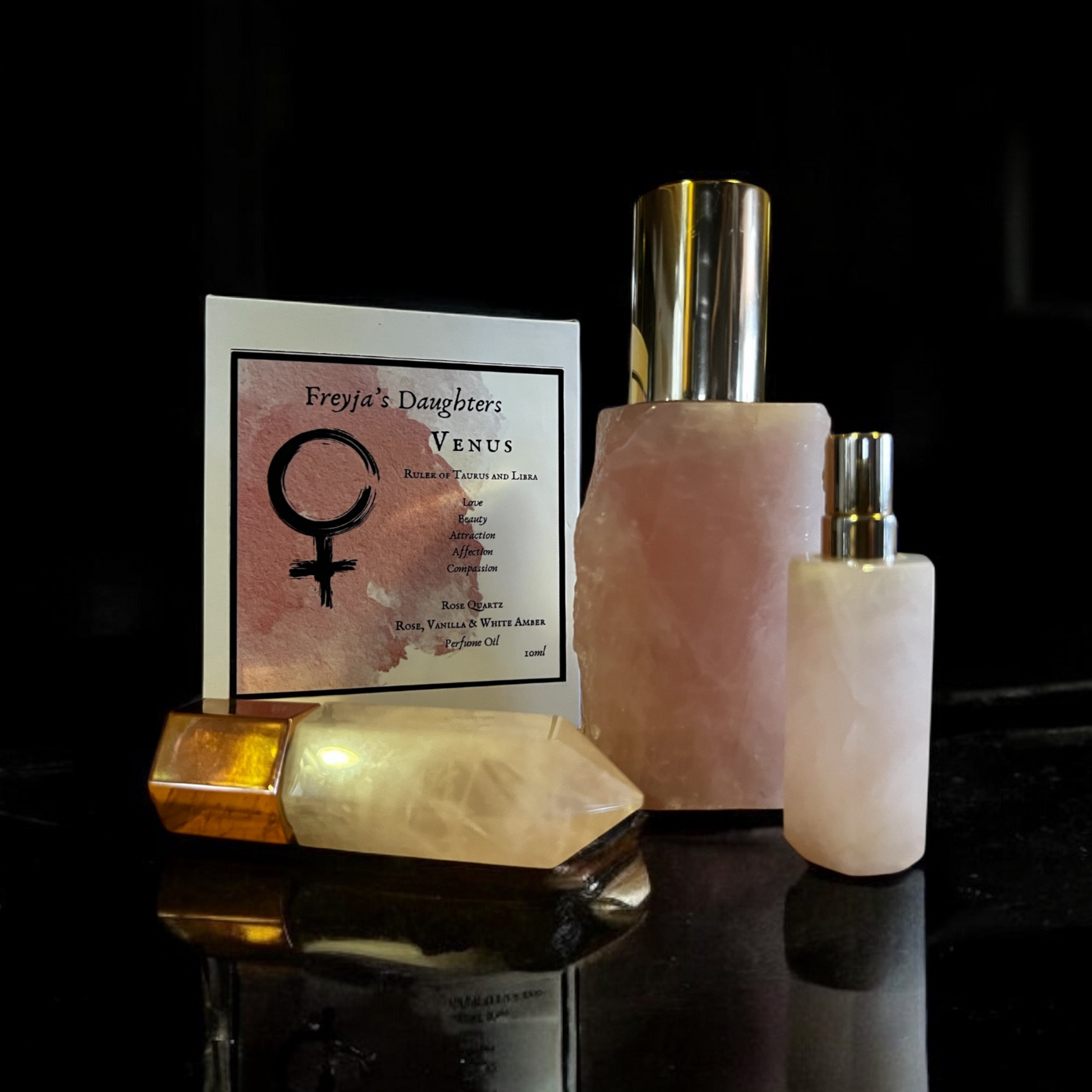 Venus Rose Quartz Perfume bottles and packaging displayed elegantly, featuring three distinct designs: a rollerball wand, a polished spray bottle, and a raw edge bottle, alongside the product's unique label.