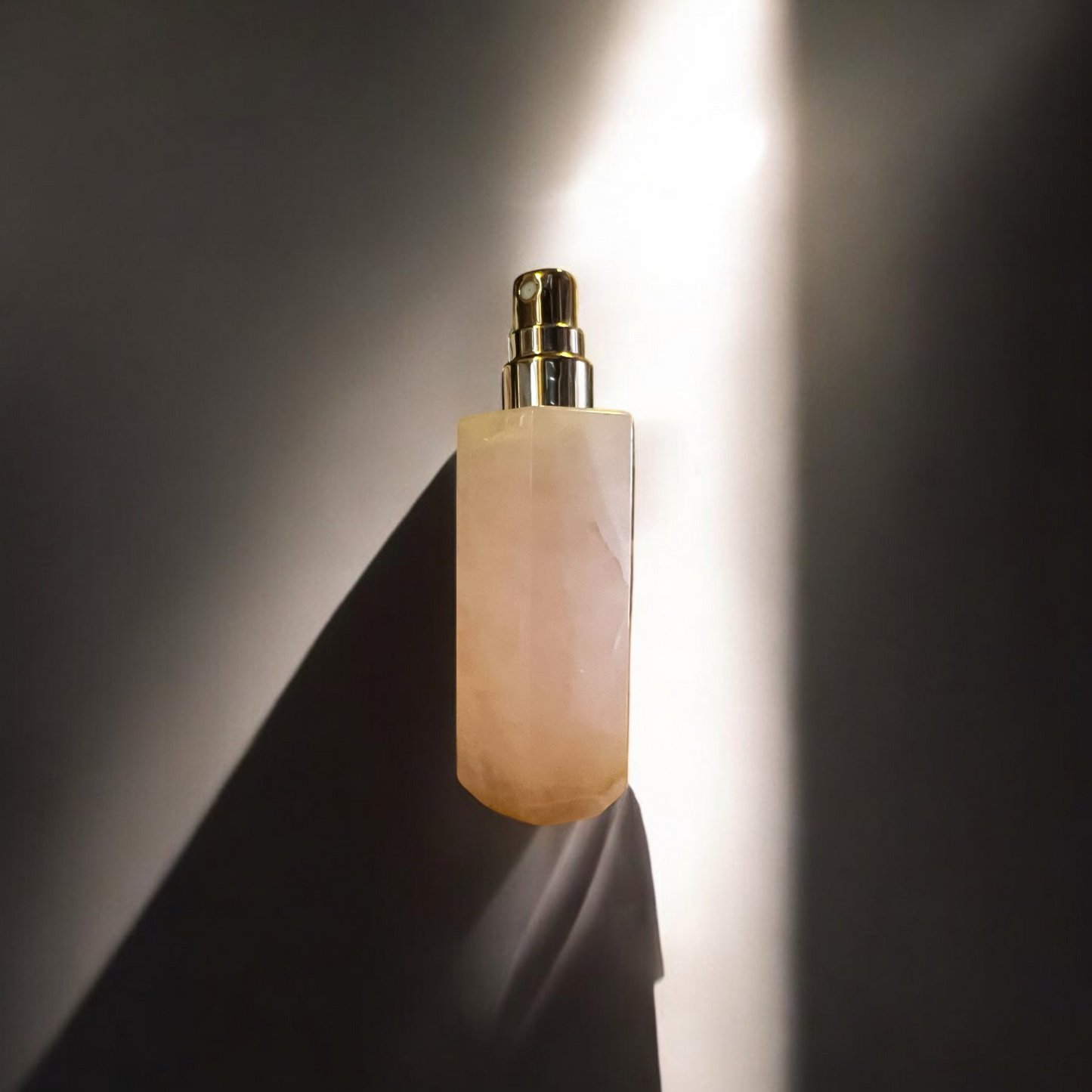 Stylish Rose Quartz spray perfume bottle positioned diagonally in soft light, showcasing its elegant shape and reflective gold details.