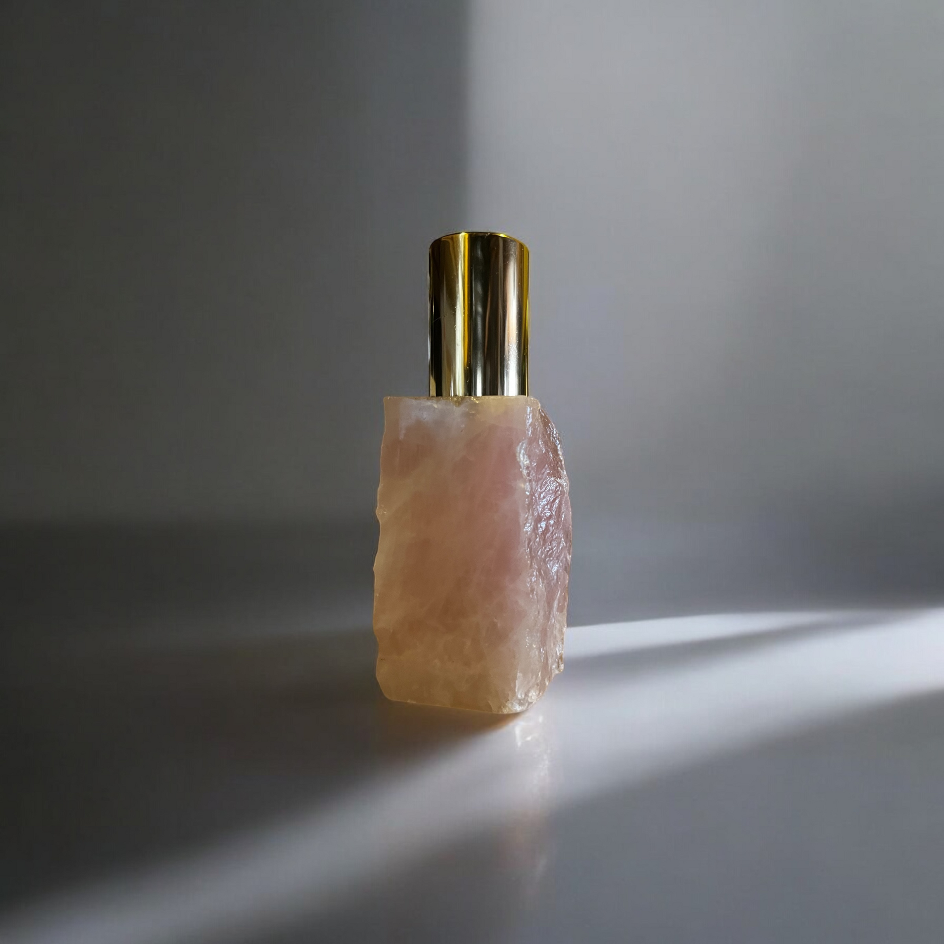 Close-up of a handcrafted Rose Quartz perfume bottle with a shiny gold cap, illuminated by soft lighting, highlighting its unique stone texture.