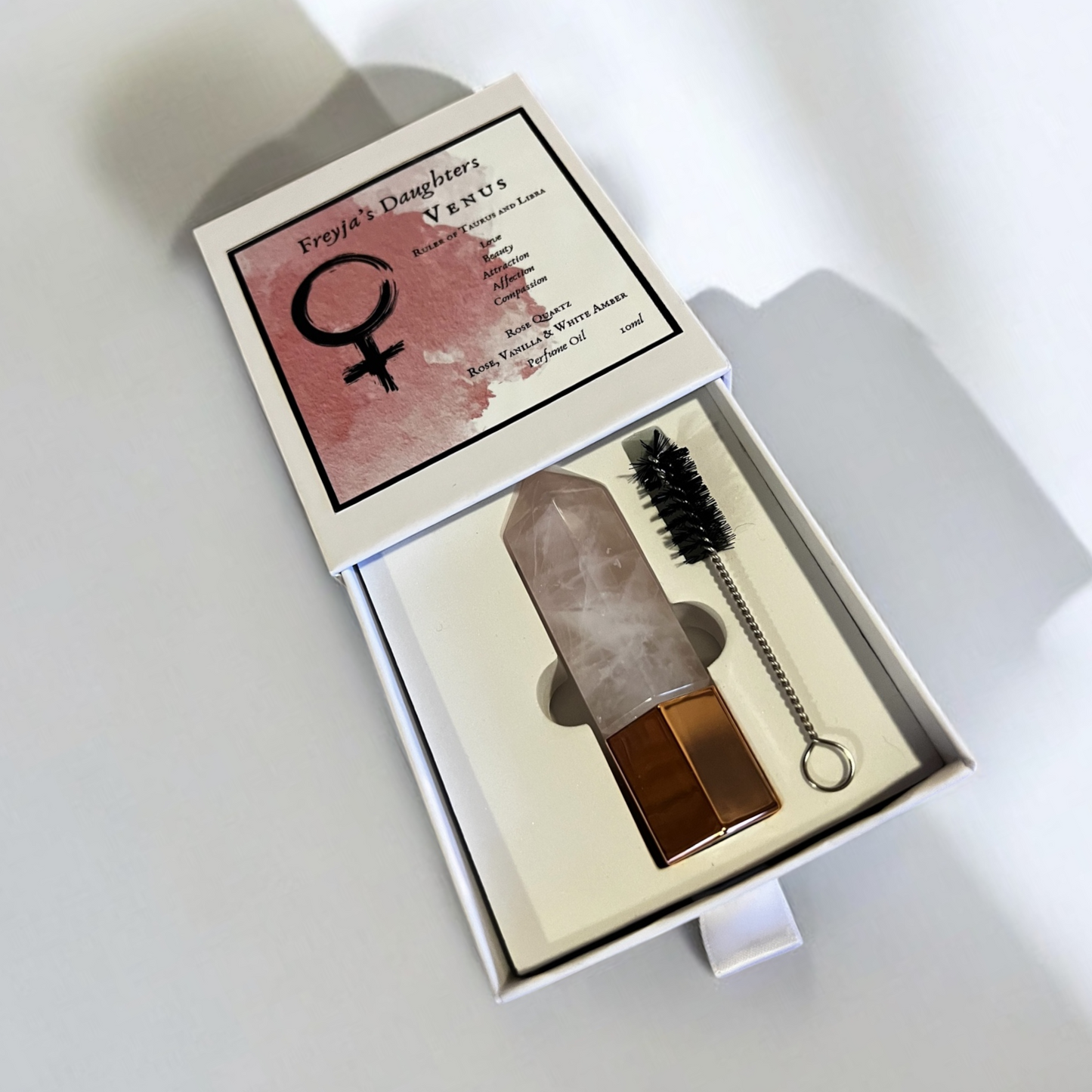 Open box displaying Venus Rose Quartz Perfume with a crystal applicator and cleaning brush, showcasing the elegant design and packaging of Freyja's Daughters.