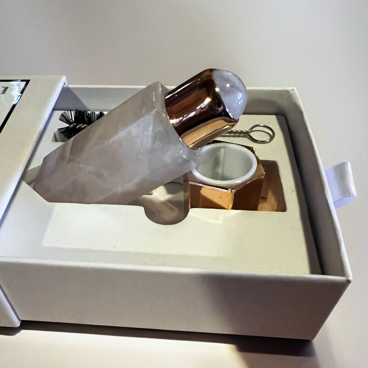 Contents of a perfume box featuring a Rose Quartz bottle with a golden top nestled in elegant packaging alongside a cleaning tool.